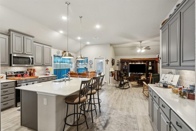 kitchen with light wood finished floors, gray cabinetry, stainless steel appliances, and vaulted ceiling