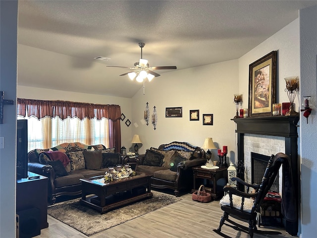 living room with light wood-type flooring, visible vents, a ceiling fan, a fireplace, and lofted ceiling