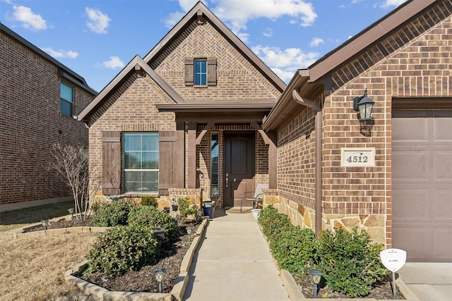 view of exterior entry with an attached garage and brick siding