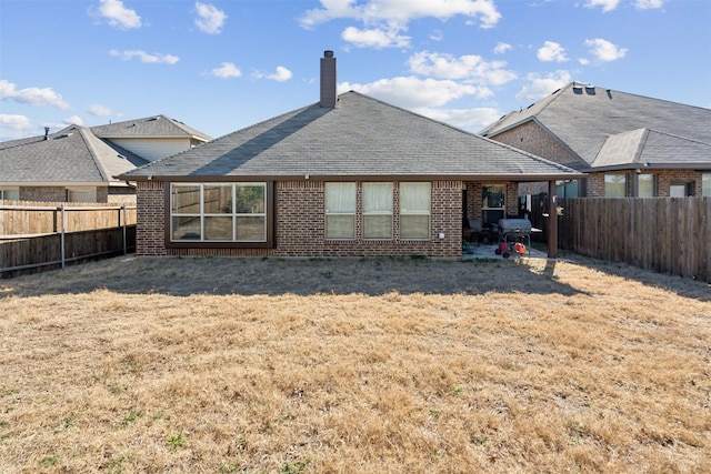 back of house with brick siding, a yard, a chimney, and a fenced backyard