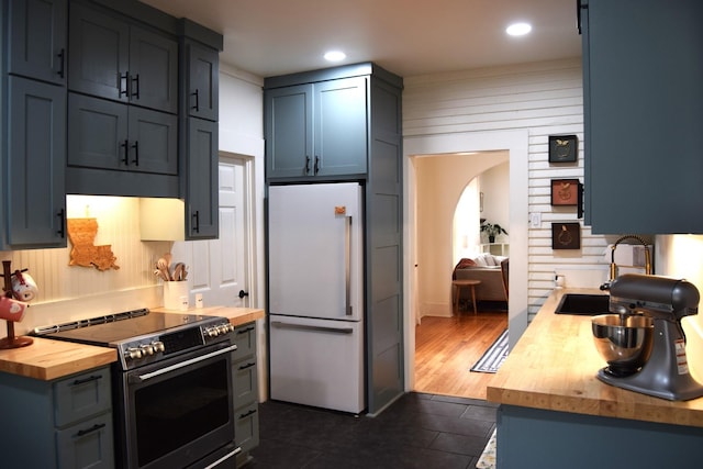 kitchen with sink, dark tile patterned floors, white refrigerator, wood counters, and stainless steel range with electric cooktop