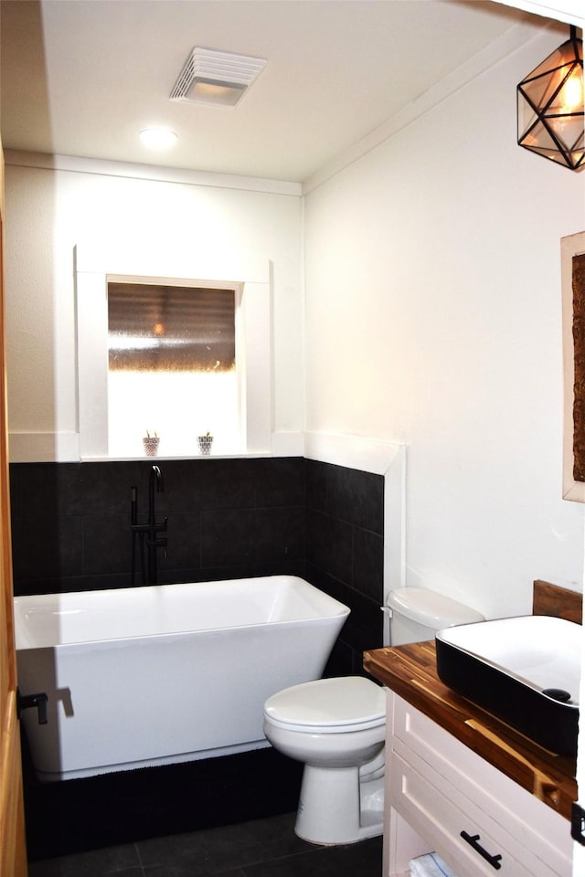 bathroom with a tub to relax in, toilet, crown molding, tile walls, and vanity