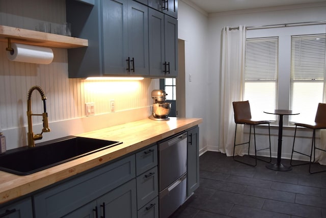 kitchen featuring wood counters, sink, crown molding, and stainless steel dishwasher