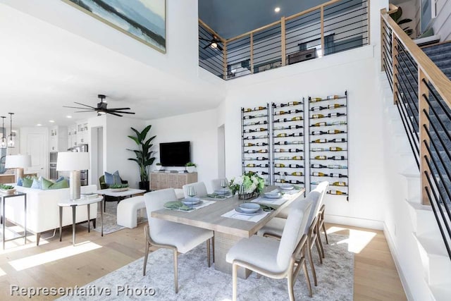 dining space with ceiling fan with notable chandelier, a towering ceiling, and light hardwood / wood-style floors