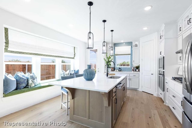 kitchen featuring appliances with stainless steel finishes, an island with sink, sink, white cabinets, and light hardwood / wood-style flooring