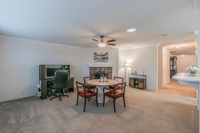 carpeted dining room with crown molding, ceiling fan, and a brick fireplace