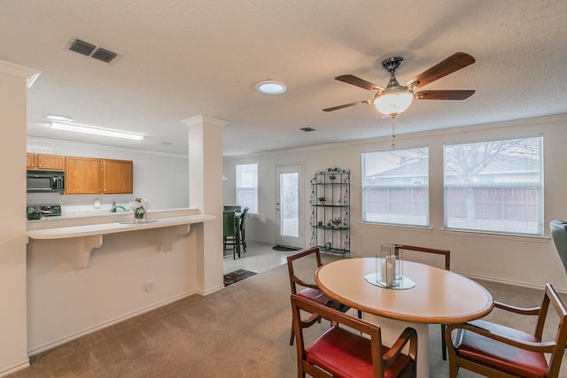 dining area featuring ornate columns, light colored carpet, a textured ceiling, ornamental molding, and ceiling fan