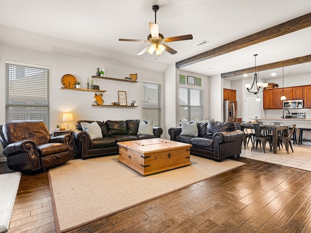 living room featuring dark wood-type flooring, ceiling fan with notable chandelier, a textured ceiling, and beam ceiling