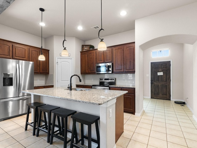 kitchen featuring an island with sink, sink, a kitchen breakfast bar, stainless steel appliances, and light stone countertops