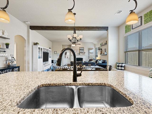 kitchen with light stone counters, an inviting chandelier, sink, and hanging light fixtures