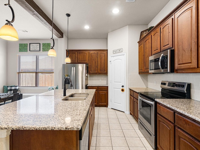 kitchen with pendant lighting, sink, stainless steel appliances, and an island with sink