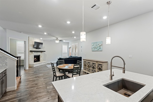 kitchen featuring a stone fireplace, sink, light stone counters, and decorative light fixtures