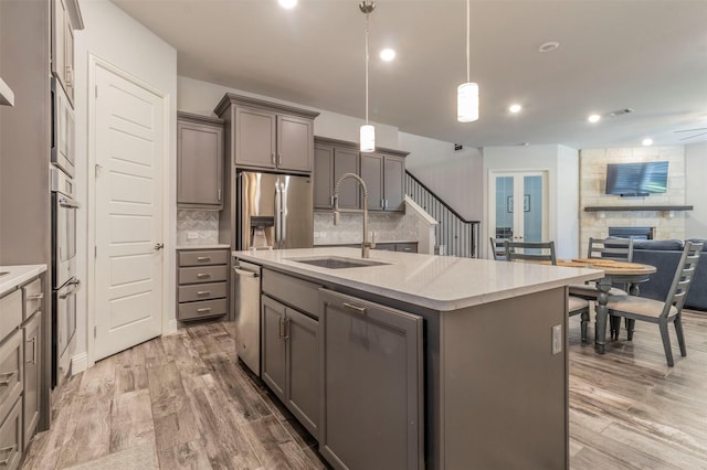 kitchen featuring stainless steel appliances, hanging light fixtures, a center island with sink, and light hardwood / wood-style flooring