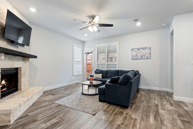 living room featuring hardwood / wood-style flooring, ceiling fan, and a stone fireplace