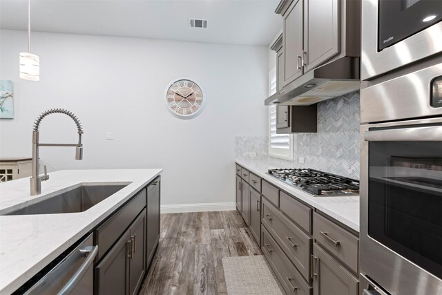 kitchen featuring pendant lighting, sink, decorative backsplash, stainless steel appliances, and light stone countertops