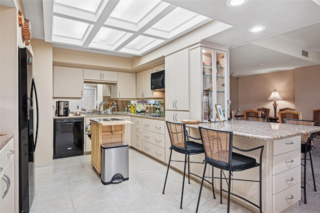 kitchen featuring cream cabinets, a breakfast bar area, black appliances, and a kitchen island