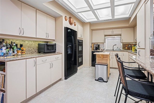 kitchen featuring sink, light tile patterned floors, backsplash, light stone countertops, and black appliances