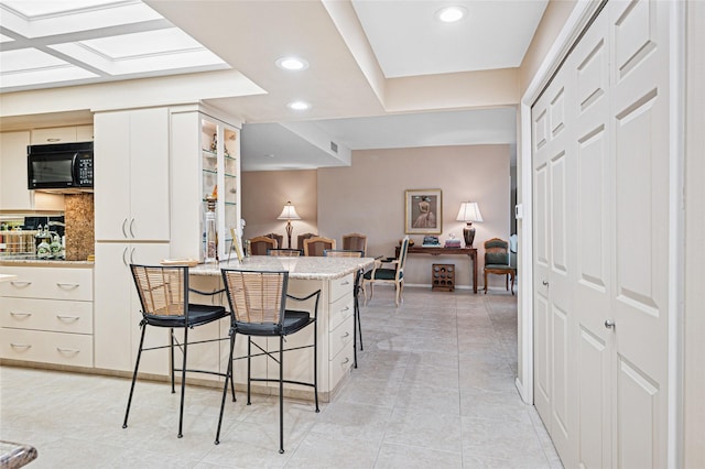 kitchen with light tile patterned floors, backsplash, a kitchen breakfast bar, and kitchen peninsula