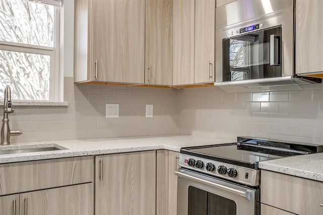 kitchen with sink, tasteful backsplash, light stone countertops, light brown cabinetry, and stainless steel range with electric cooktop