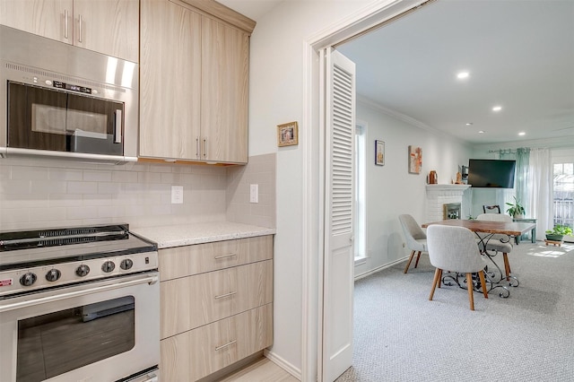 kitchen featuring stainless steel appliances, tasteful backsplash, light brown cabinetry, a brick fireplace, and light colored carpet