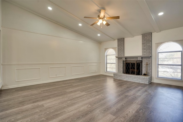 unfurnished living room with a brick fireplace, a wealth of natural light, lofted ceiling with beams, and hardwood / wood-style floors