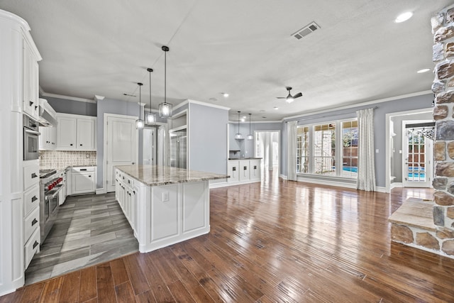 kitchen with pendant lighting, stainless steel appliances, a center island, light stone countertops, and white cabinets