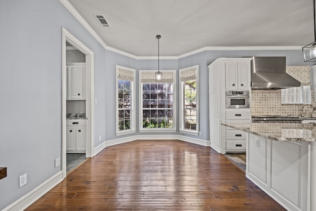 kitchen featuring pendant lighting, white cabinets, stainless steel appliances, and wall chimney range hood