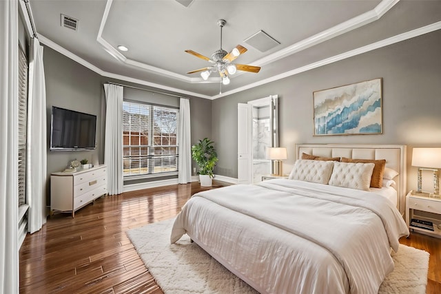 bedroom featuring dark wood-type flooring, ceiling fan, ornamental molding, and a tray ceiling