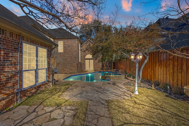 pool at dusk with an in ground hot tub, a patio area, and a lawn