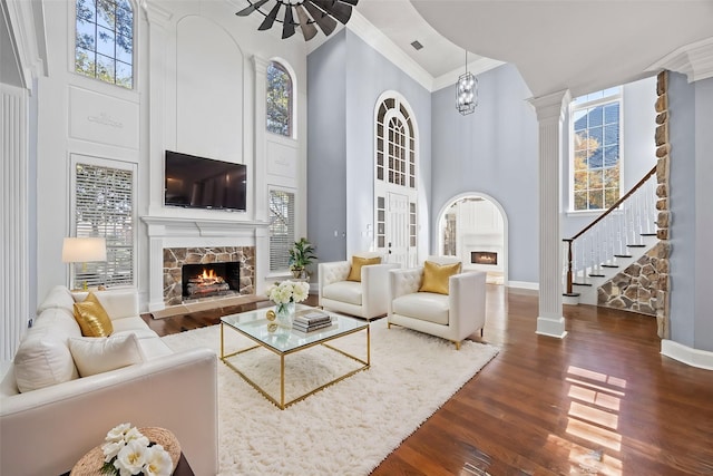 living room featuring dark wood-type flooring, ornamental molding, a towering ceiling, a healthy amount of sunlight, and a fireplace