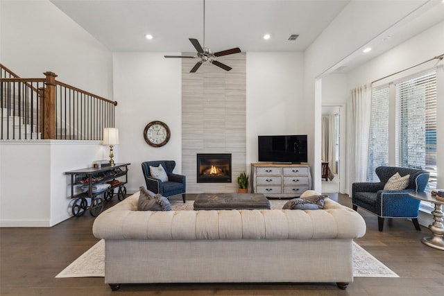 living room featuring ceiling fan, a fireplace, dark hardwood / wood-style flooring, and a towering ceiling