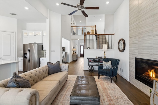 living room featuring a tiled fireplace, a high ceiling, dark hardwood / wood-style floors, and ceiling fan