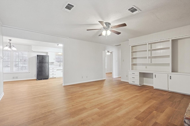 unfurnished living room featuring ceiling fan with notable chandelier, built in desk, a textured ceiling, and light wood-type flooring