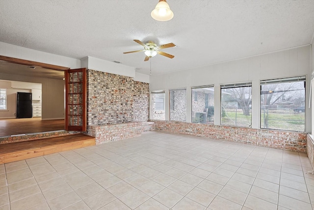 unfurnished living room featuring light tile patterned flooring, brick wall, a textured ceiling, and ceiling fan