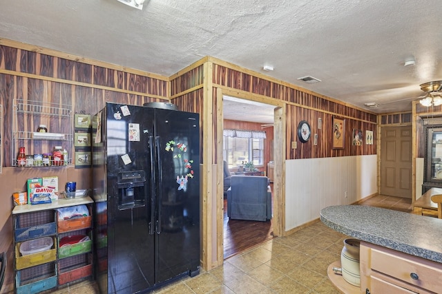 kitchen featuring wooden walls, a textured ceiling, and black fridge with ice dispenser