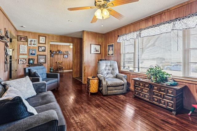 living room featuring ceiling fan, dark wood-type flooring, wooden walls, and a textured ceiling