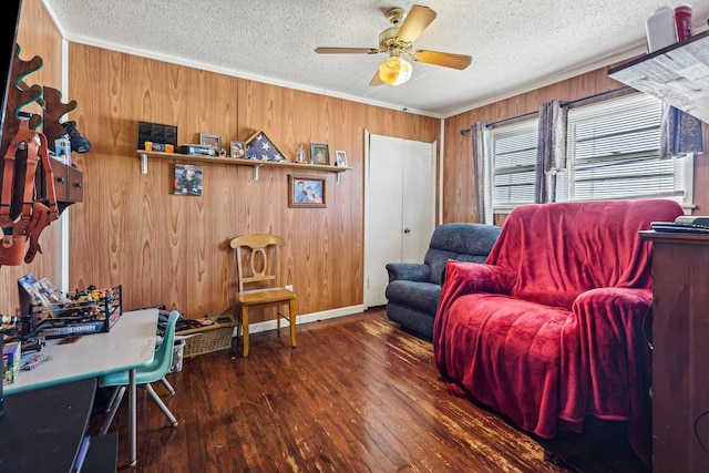 living room with wooden walls, dark hardwood / wood-style flooring, ornamental molding, ceiling fan, and a textured ceiling