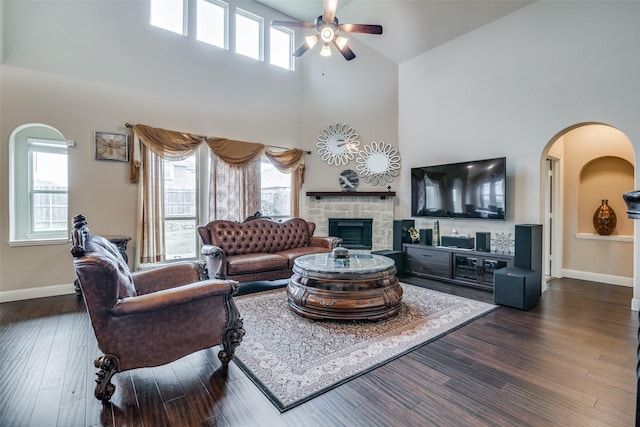 living room featuring a high ceiling, a stone fireplace, dark hardwood / wood-style floors, and ceiling fan