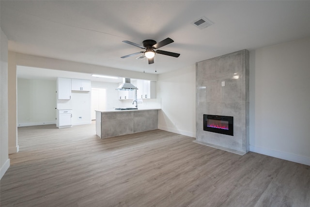 unfurnished living room with a tiled fireplace, ceiling fan, sink, and light wood-type flooring