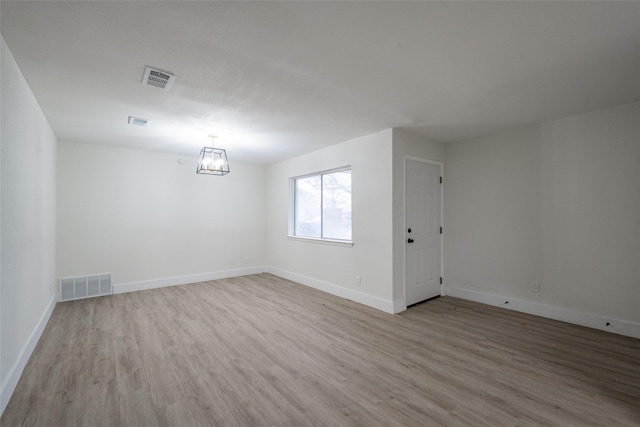 empty room with a notable chandelier and light hardwood / wood-style floors