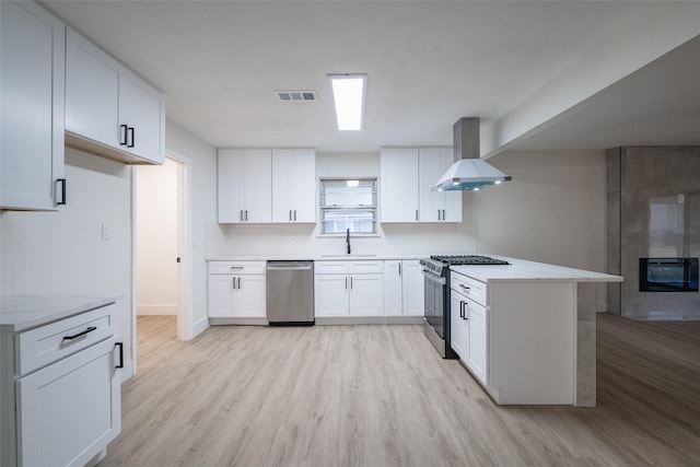 kitchen featuring extractor fan, appliances with stainless steel finishes, white cabinetry, sink, and light hardwood / wood-style floors