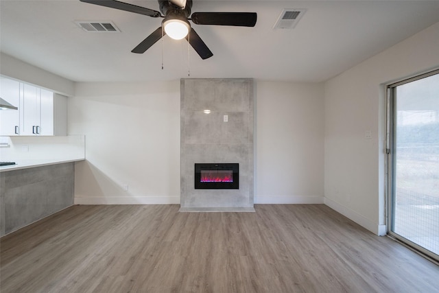 unfurnished living room featuring ceiling fan, a tiled fireplace, and light hardwood / wood-style flooring