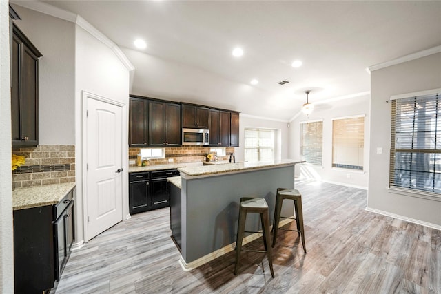 kitchen with a kitchen breakfast bar, ornamental molding, a kitchen island, and light stone counters