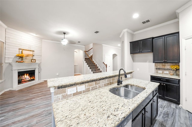 kitchen featuring sink, ornamental molding, light stone countertops, a kitchen island with sink, and decorative backsplash