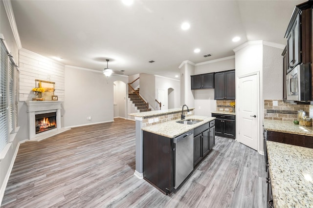 kitchen with appliances with stainless steel finishes, sink, a kitchen island with sink, light stone countertops, and light hardwood / wood-style flooring