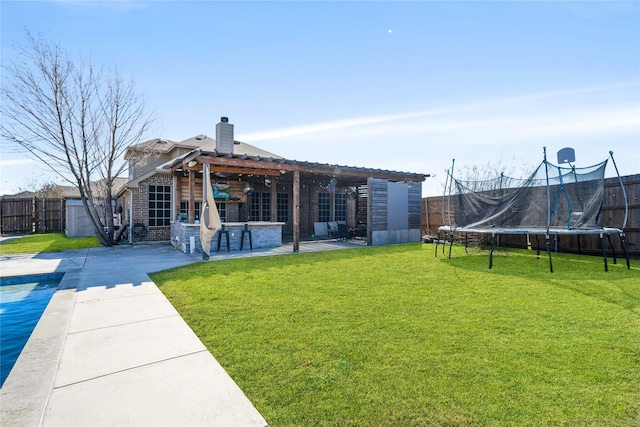 rear view of house with a yard, a patio area, and a trampoline