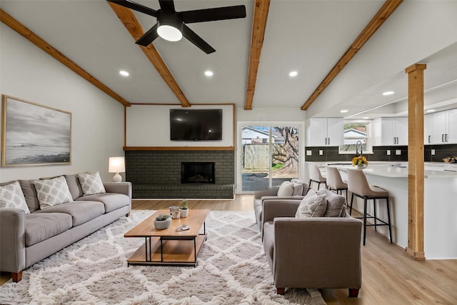 living room with vaulted ceiling with beams, light hardwood / wood-style flooring, ceiling fan, a fireplace, and decorative columns