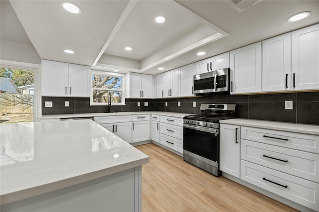 kitchen featuring appliances with stainless steel finishes, a raised ceiling, light hardwood / wood-style flooring, and white cabinets