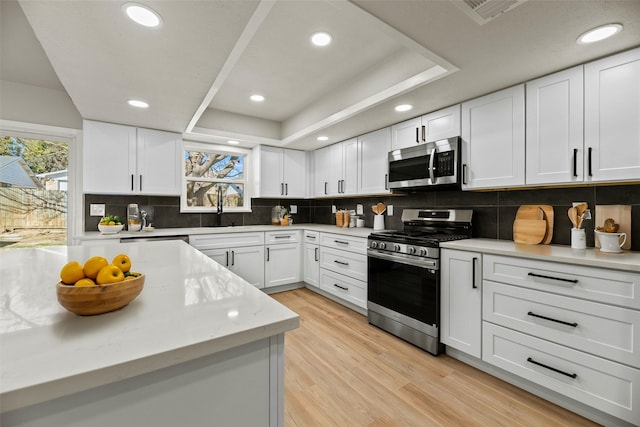 kitchen featuring white cabinetry, light hardwood / wood-style flooring, appliances with stainless steel finishes, plenty of natural light, and a raised ceiling