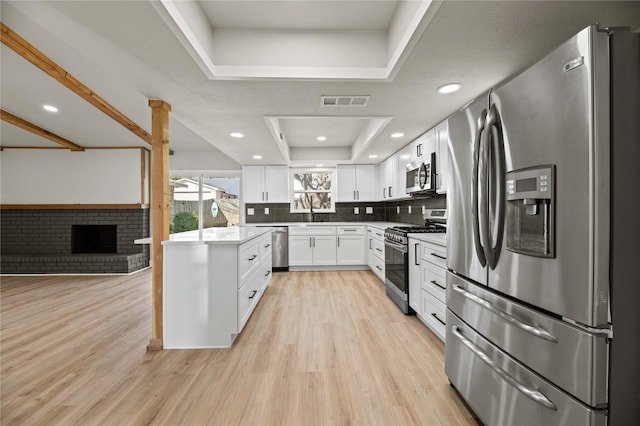 kitchen featuring white cabinetry, tasteful backsplash, light hardwood / wood-style flooring, a tray ceiling, and stainless steel appliances